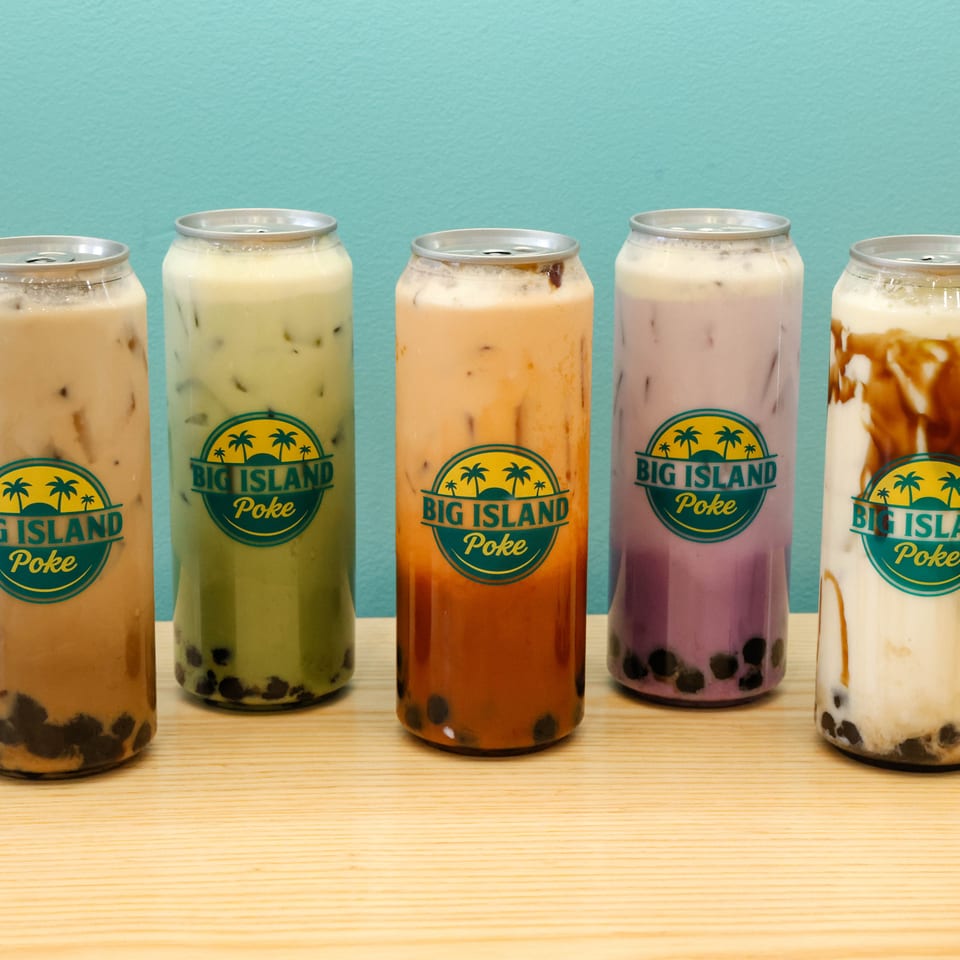 Five colorful Big Island Poke bubble teas with tapioca pearls displayed on a wooden table against a turquoise wall.