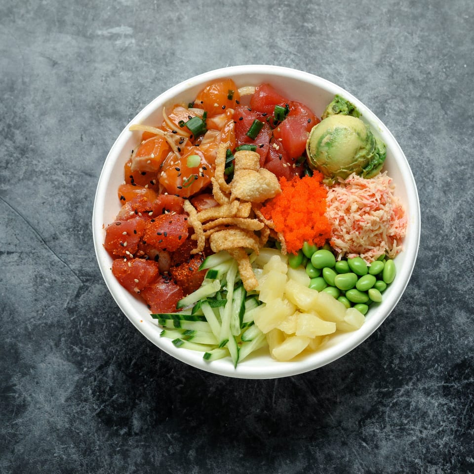 Colorful poke bowl topped with raw tuna and salmon, avocado, edamame, cucumber, pineapple, crab salad, and crispy wonton strips.