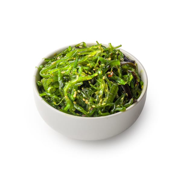 A white bowl filled with bright green seaweed salad, sprinkled with sesame seeds.