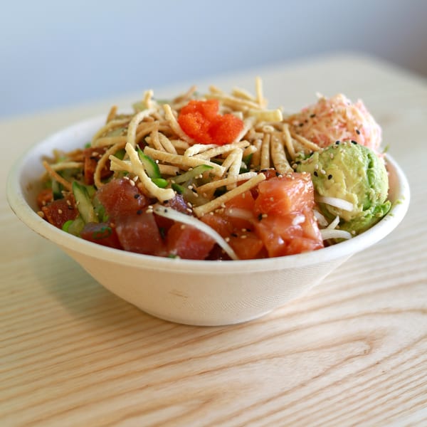 Big Island Poke bowl with tuna, salmon, avocado, crispy noodles, and roe on a wooden table.